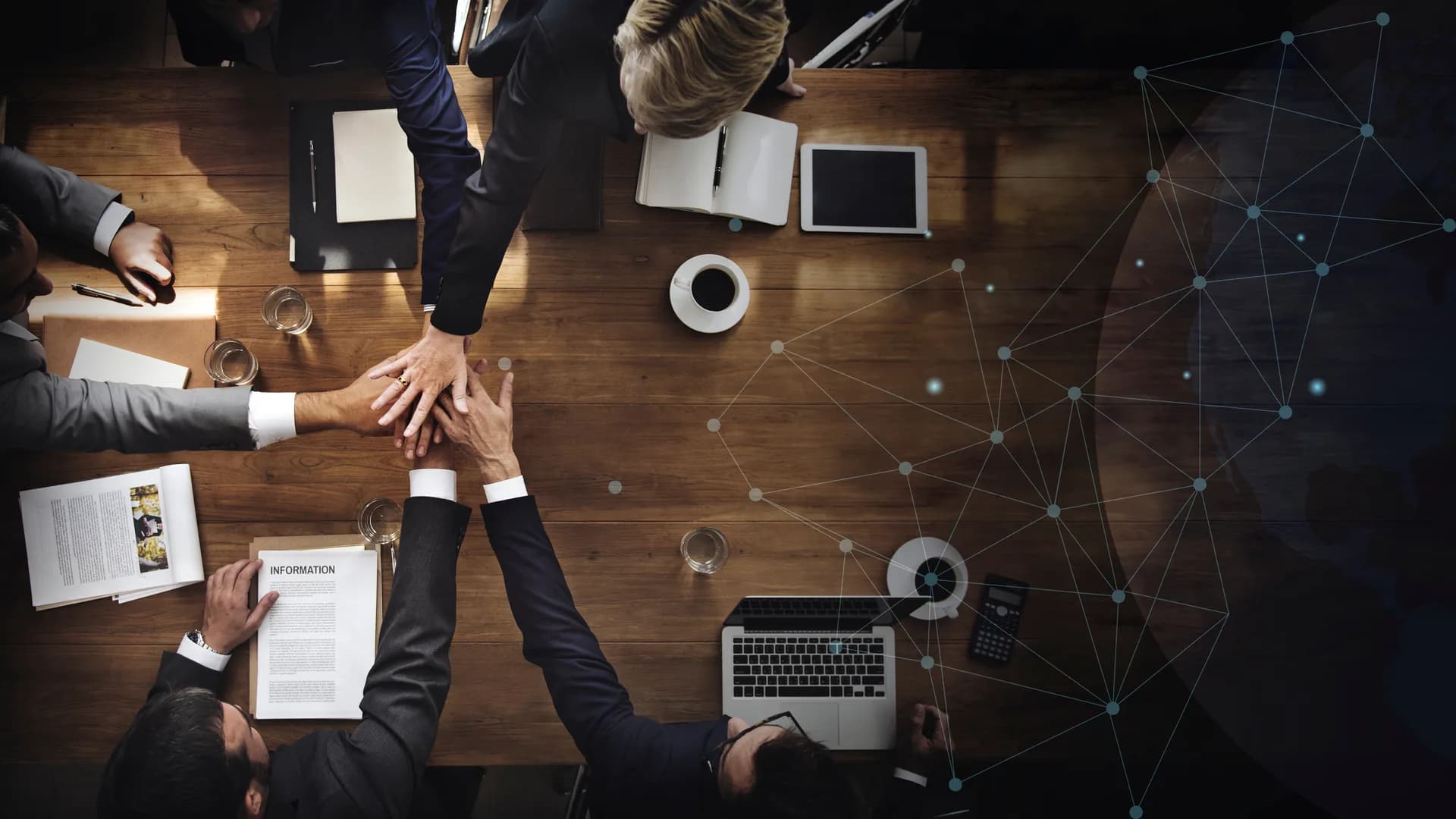 Team celebrating with a high five over a business meeting table, overlaid with a network graphic